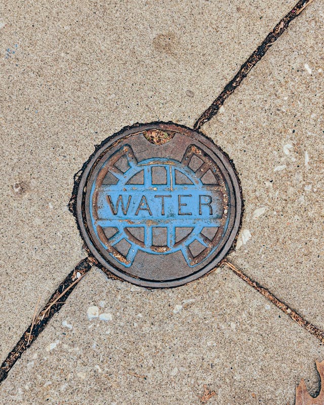 Round water manhole cover set in concrete pavement with visible joints